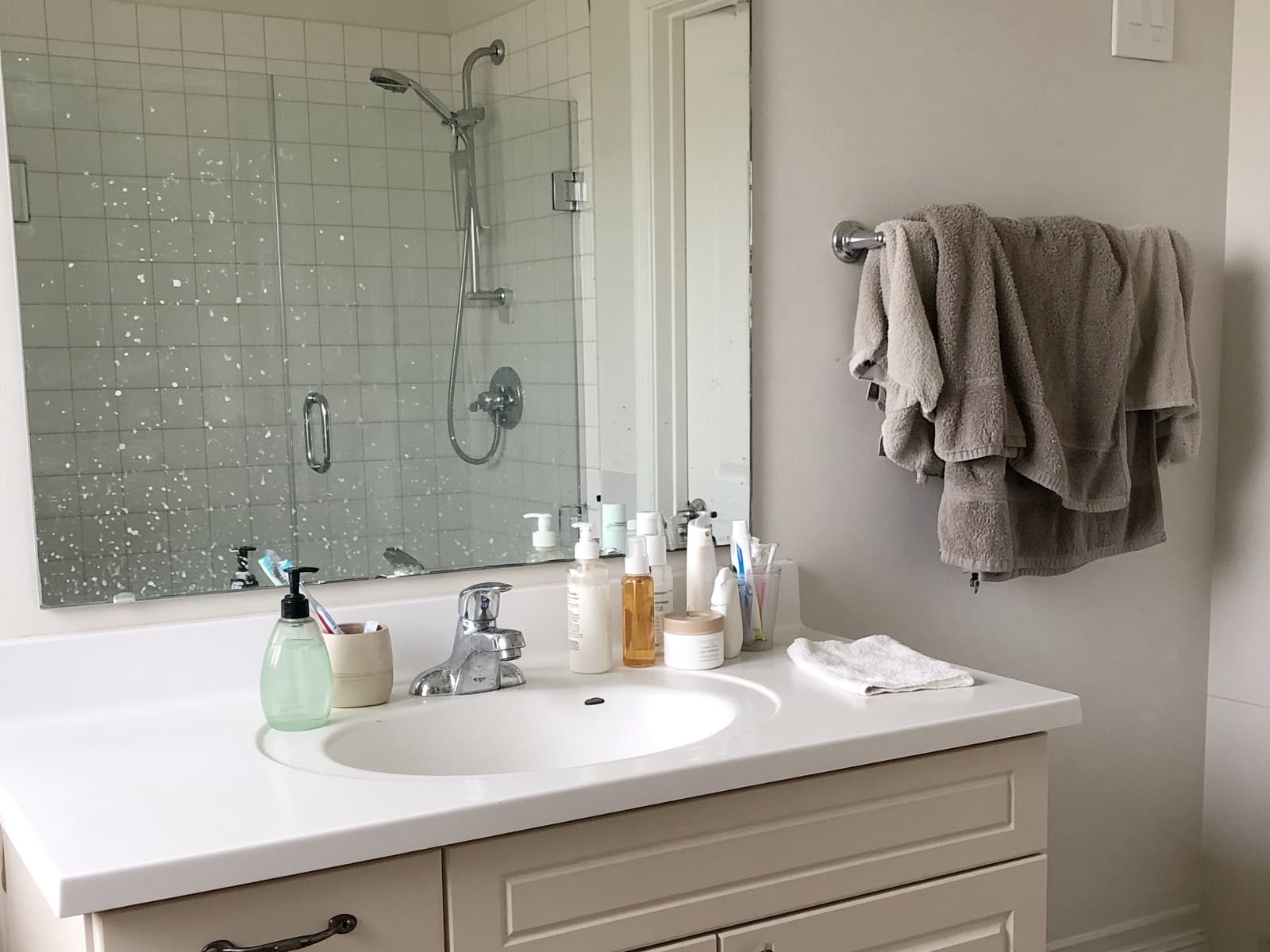 Lived-in bathroom before cleaning, with clustered bottles and a dull mirror
